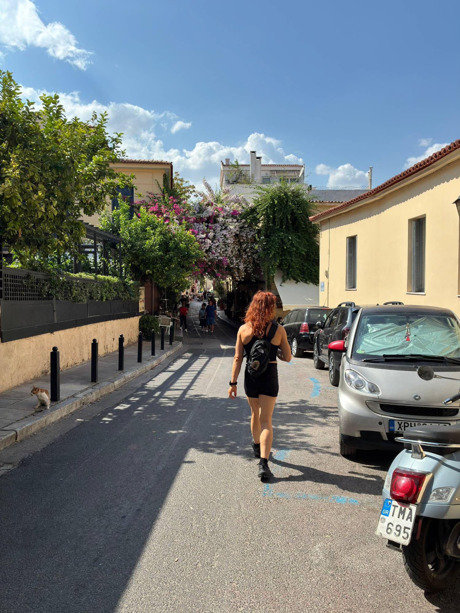 Kristine walking down a street in Plaka towards a canopy of pink and white bougainvillea