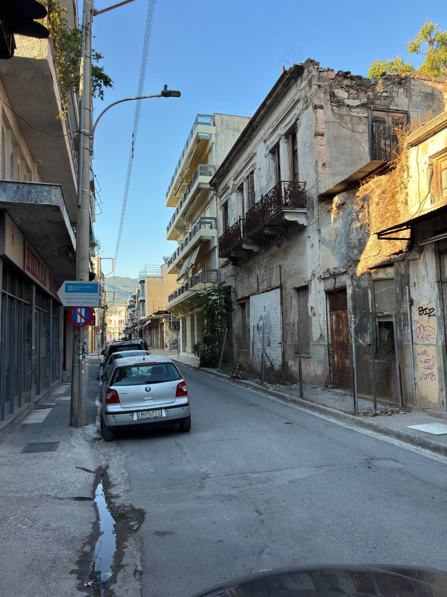 A quiet back street in Kalamata with a crumbling old two-storey building beside a modern apartment block