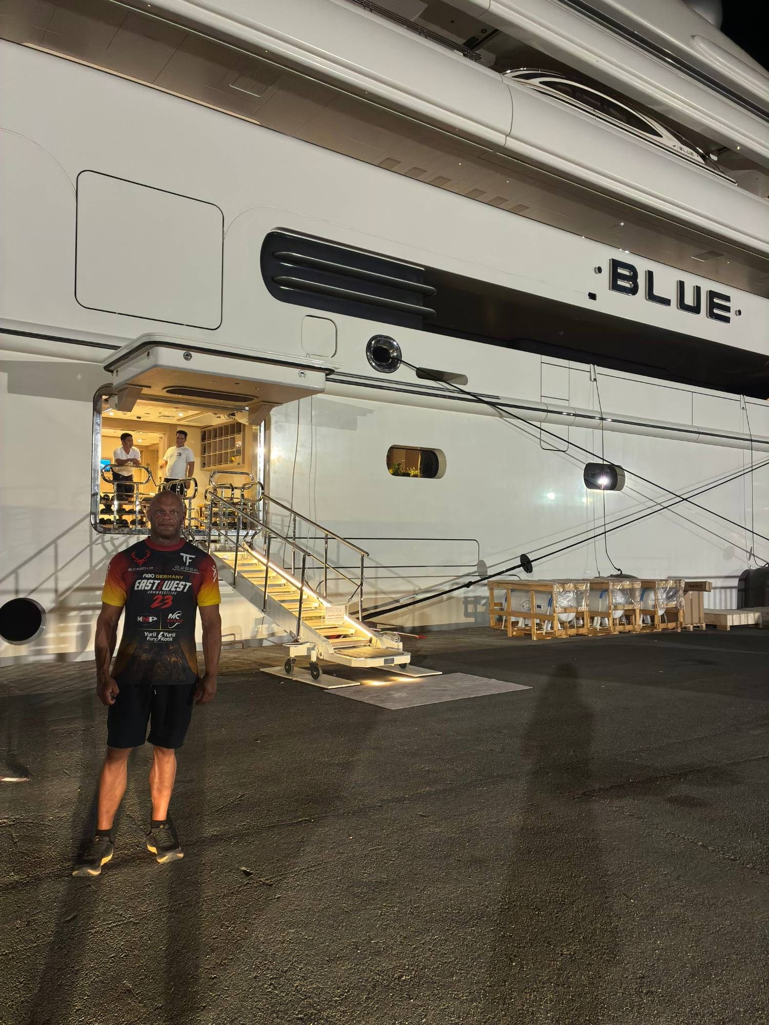 Standing on the quay at night beside the hull of the superyacht Blue, with the crew door open and lit