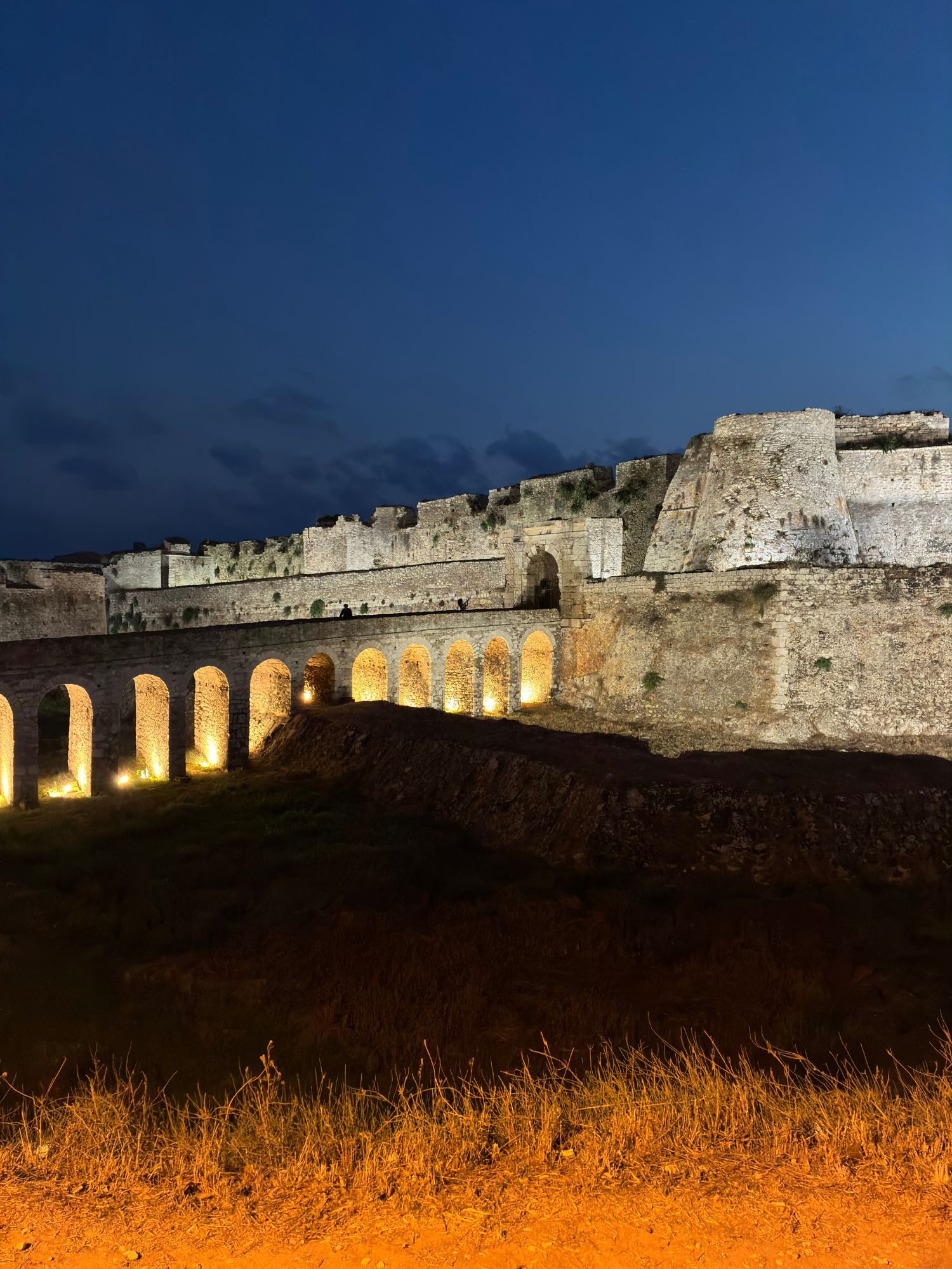 The illuminated arched stone bridge leading to the main gate of Methoni Castle at night