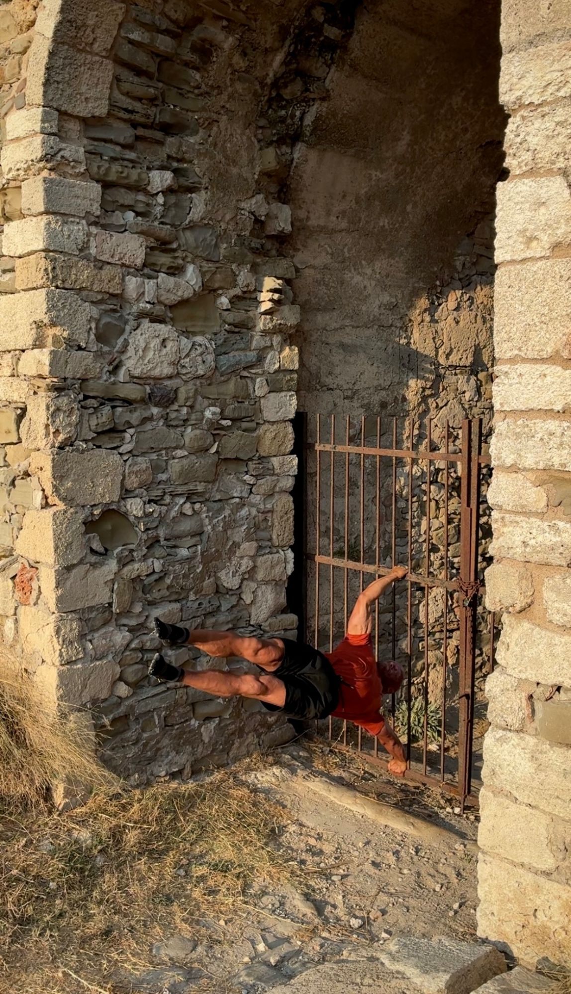 Doing a human flag on an old iron gate inside Methoni Castle
