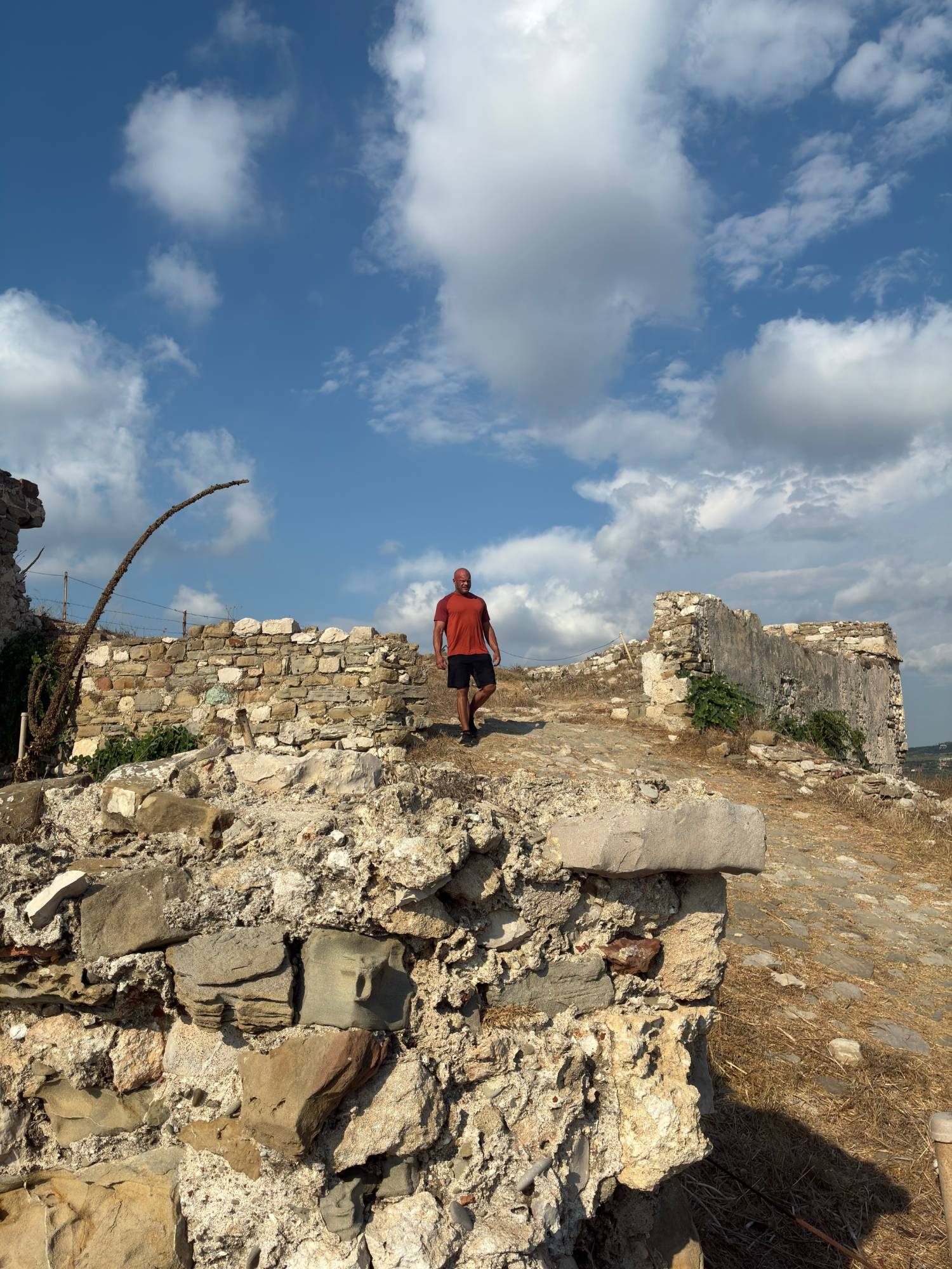 Walking along an old cobbled path through the ruins inside Methoni Castle under a cloudy blue sky