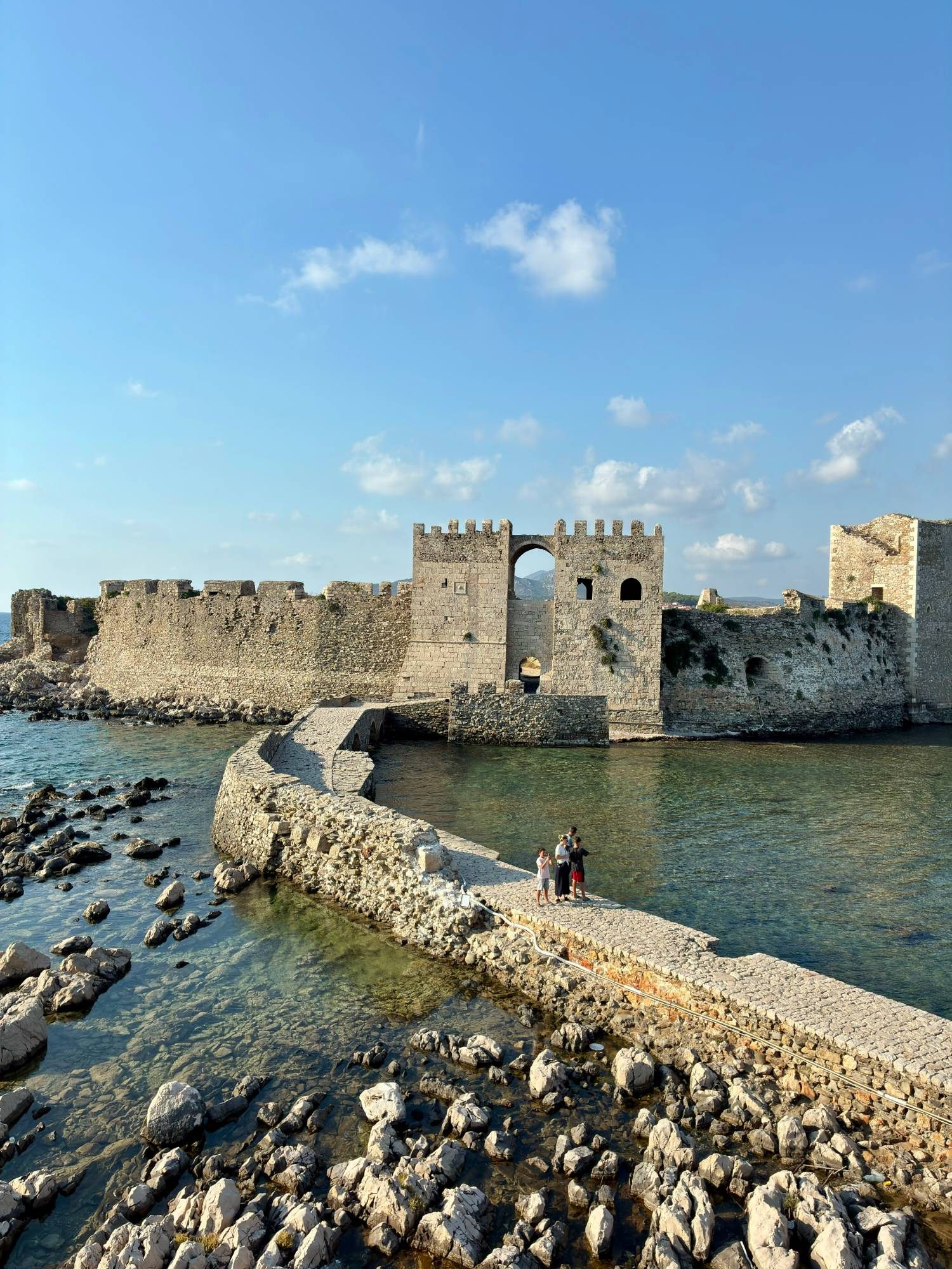 The sea gate and walls of Methoni Castle with the stone causeway crossing clear water