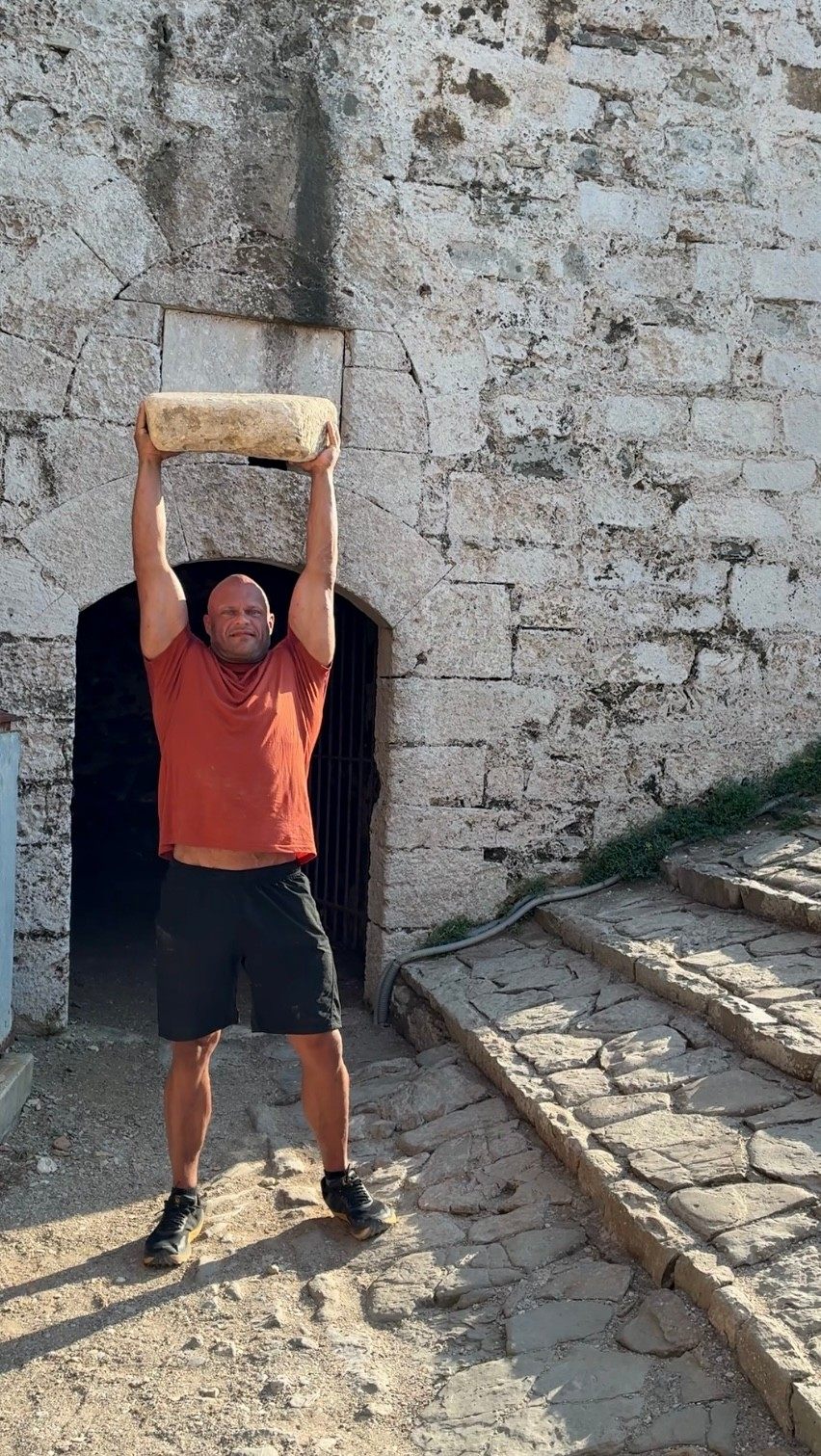 Holding a big stone overhead in front of an old gateway in the walls of Methoni Castle
