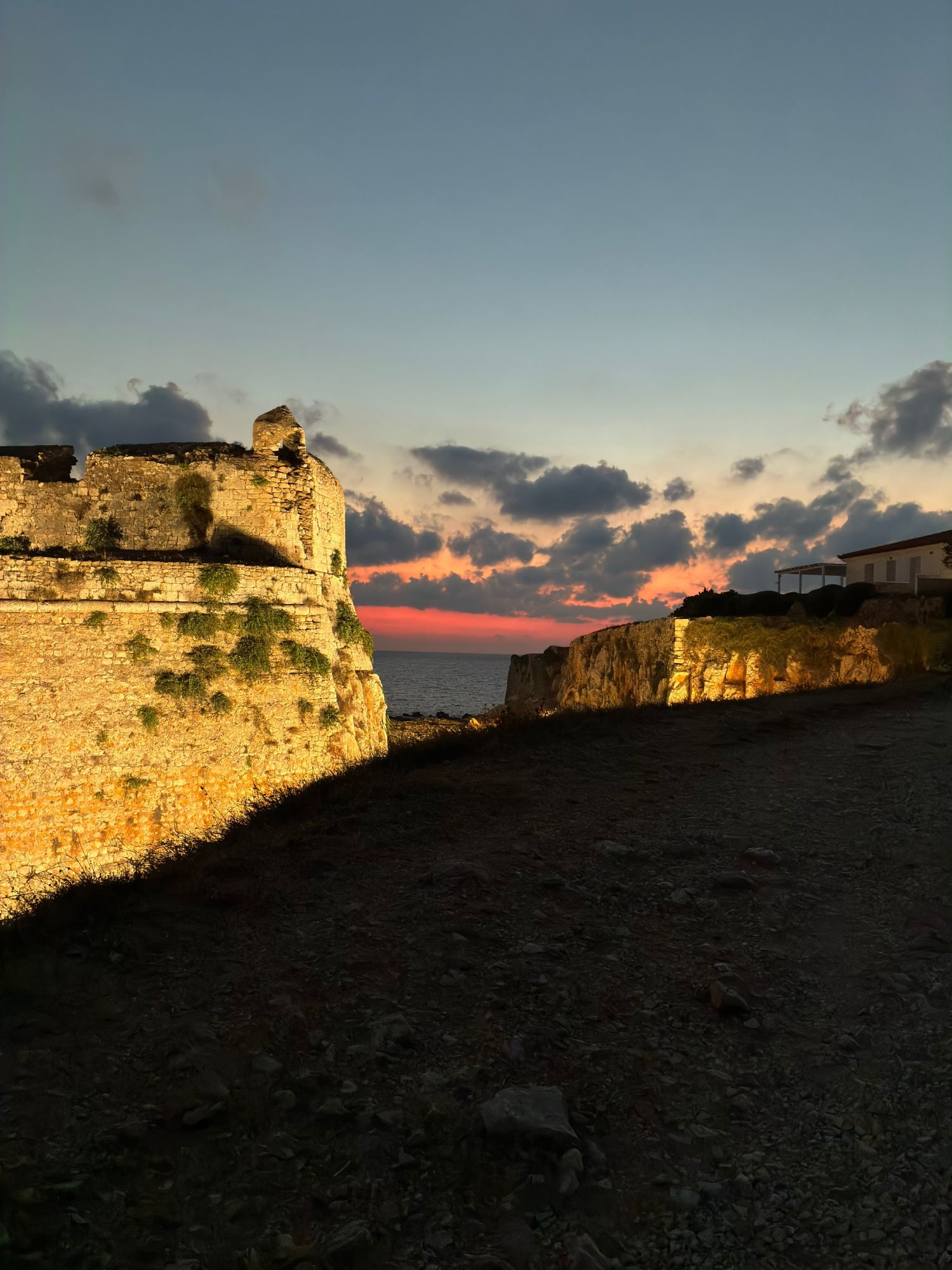 Floodlit corner of Methoni Castle's walls with a pink sunset over the sea beyond