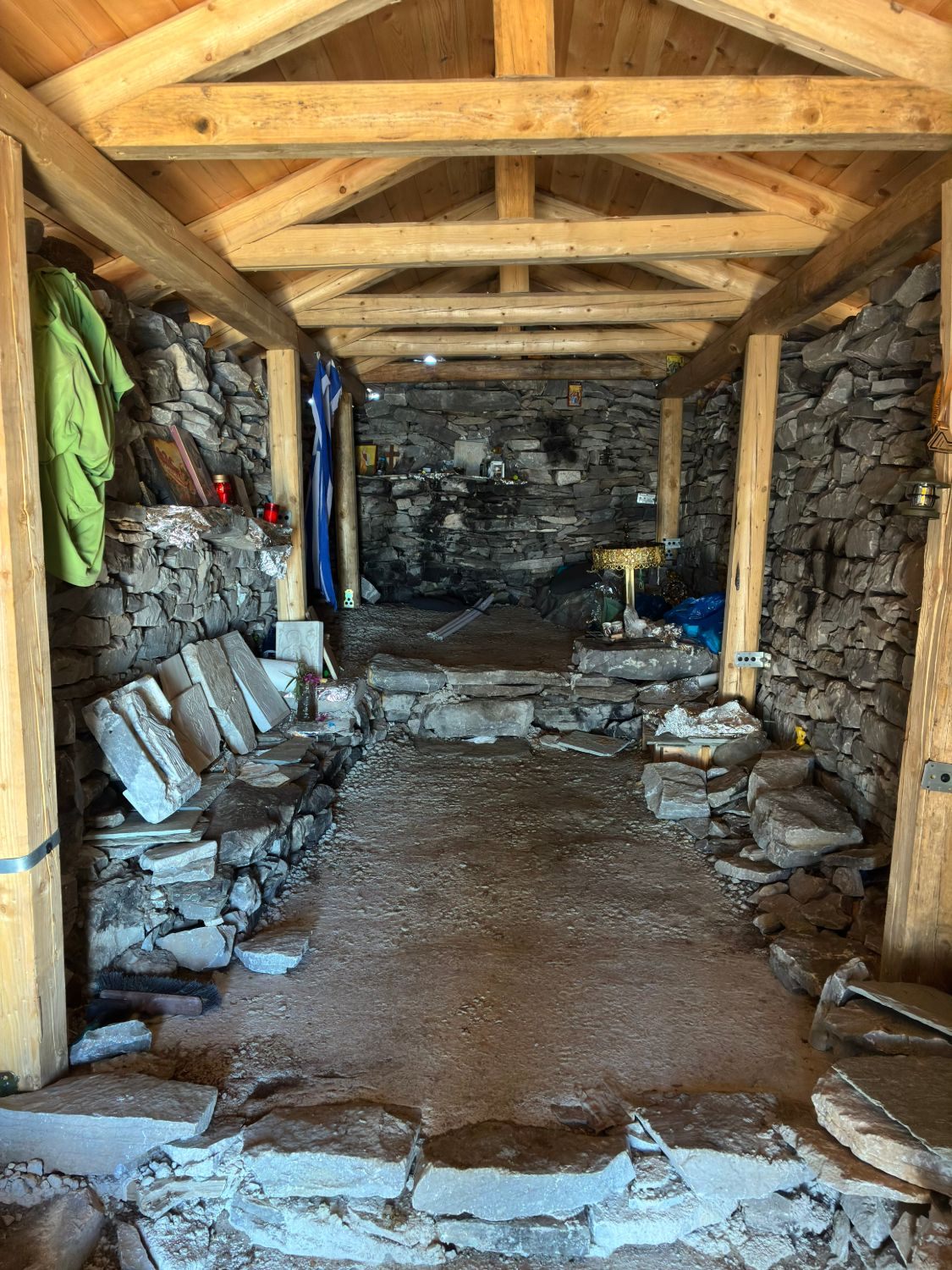 Inside the small stone chapel on Profitis Ilias, with dry-stone walls, wooden roof beams, icons, candles and a Greek flag
