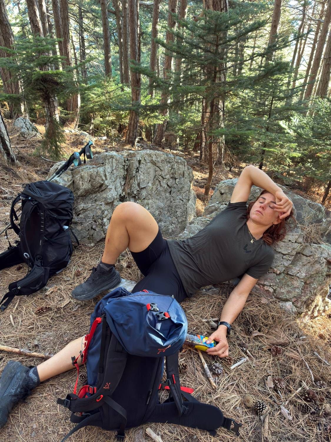 Kristine lying exhausted against a rock in the pine forest on the lower slopes of Mount Taygetos, backpacks beside her