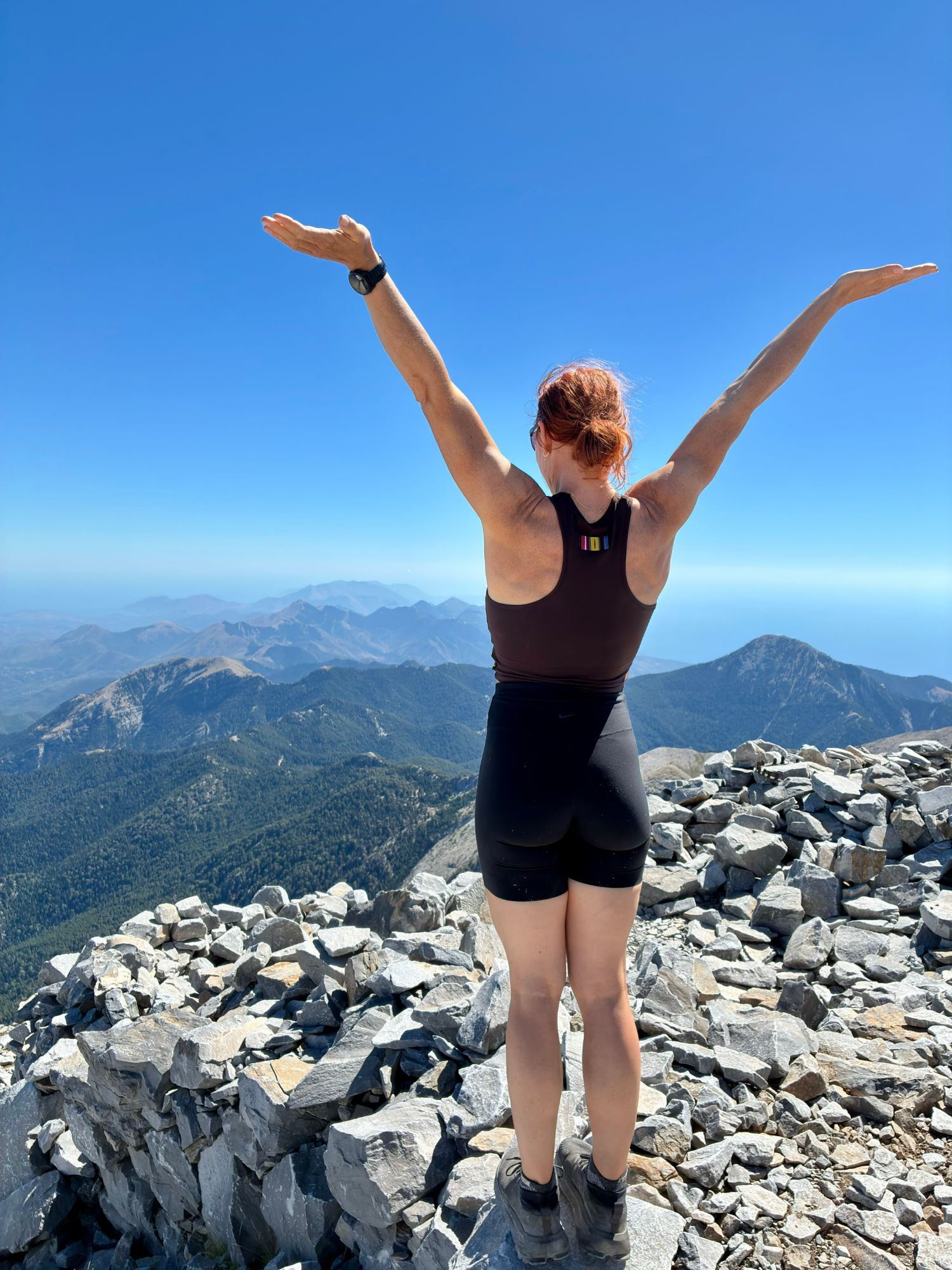 Kristine with her arms outstretched on the summit of Mount Taygetos, with the view behind her