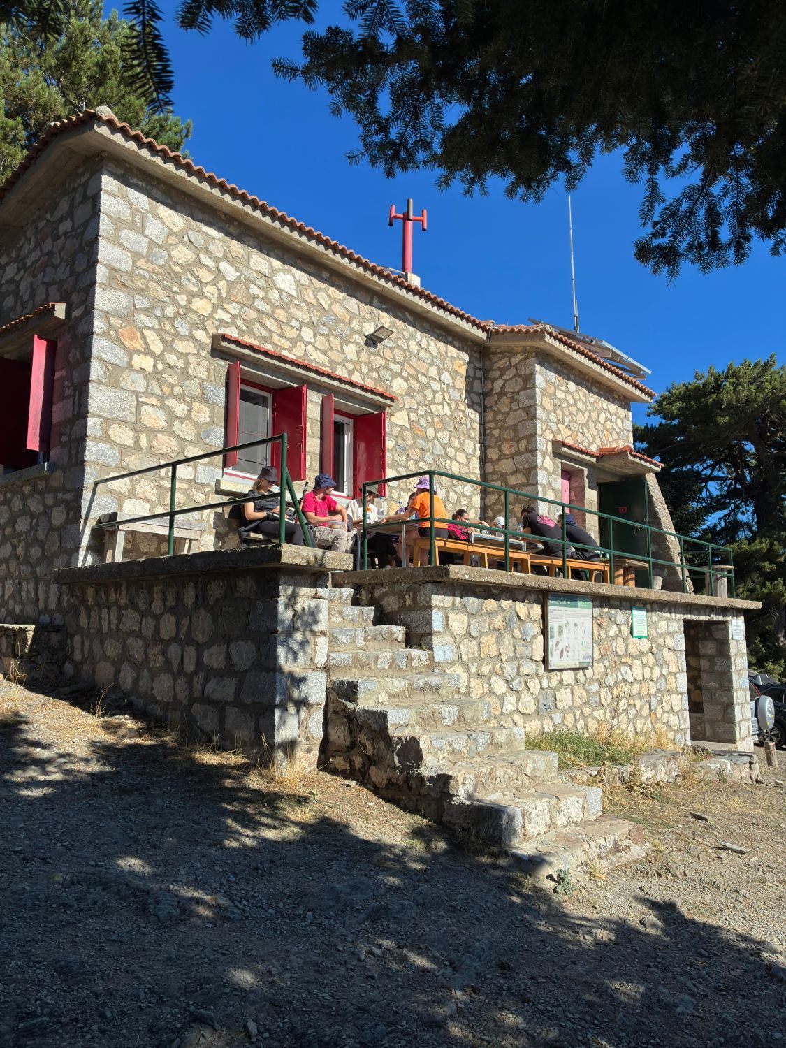 Hikers sitting at tables on the terrace of the stone-built Taygetos Refuge in the morning sun