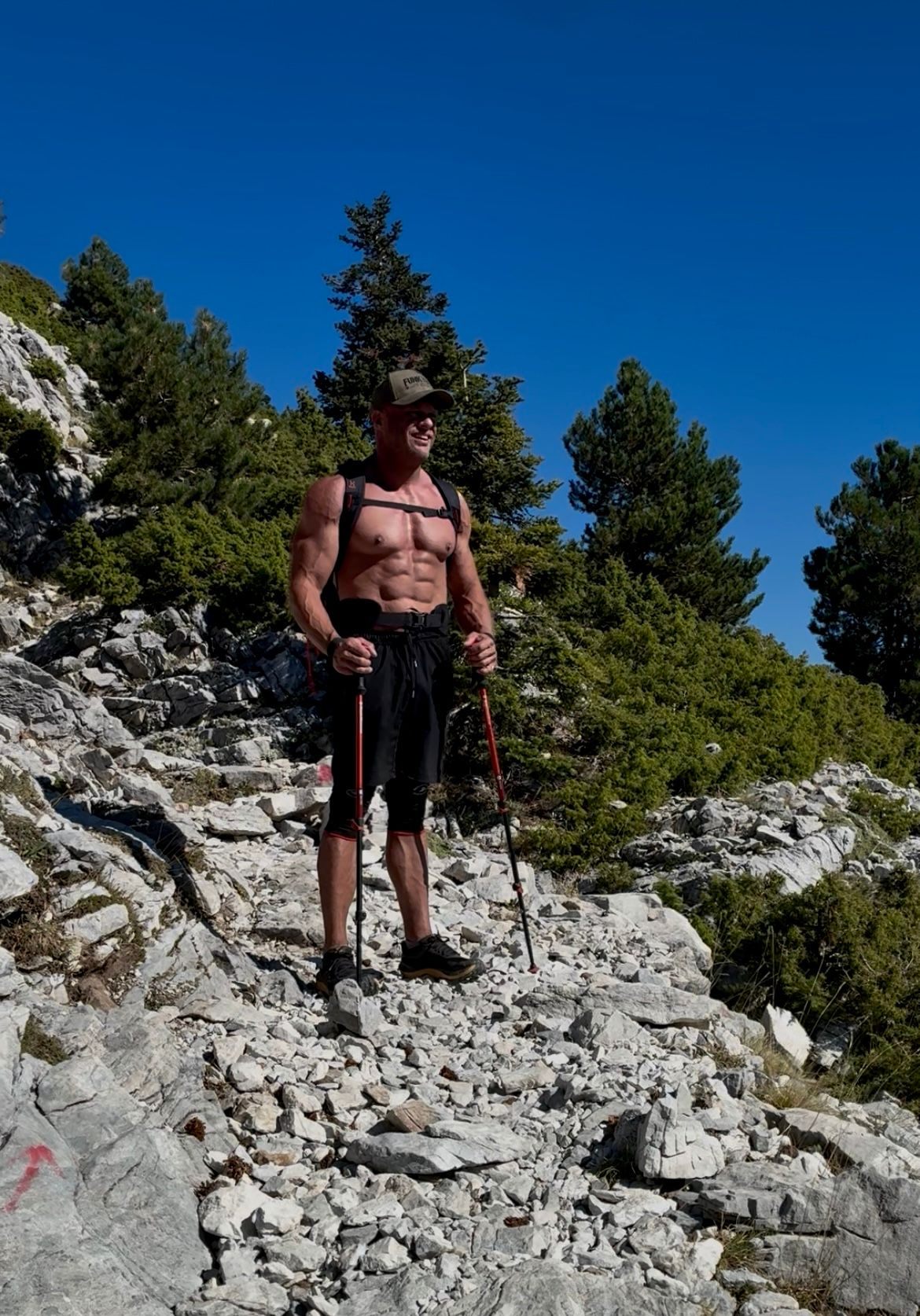 Hiking with trekking poles on a rocky trail among the last pines on Mount Taygetos, with a red trail marking on the rock