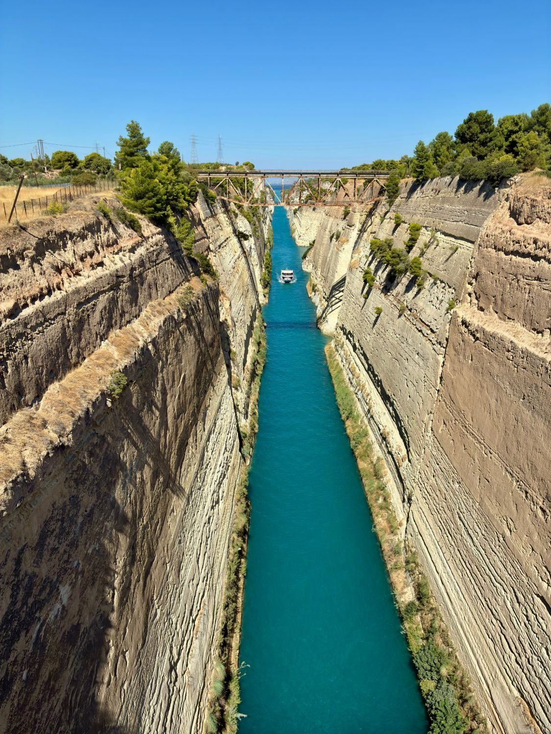 Looking down into the Corinth Canal from the bridge, with a boat sailing between the sheer rock walls