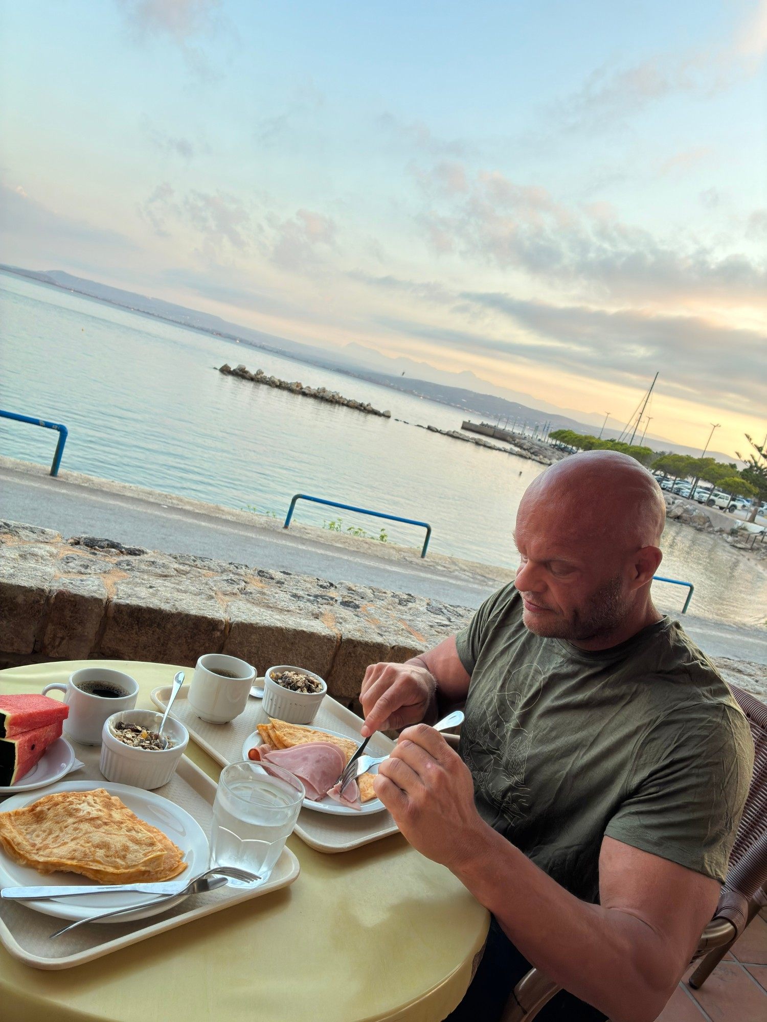 Breakfast with crêpes, ham, muesli, watermelon and coffee at a table by the sea in Pylos at dawn