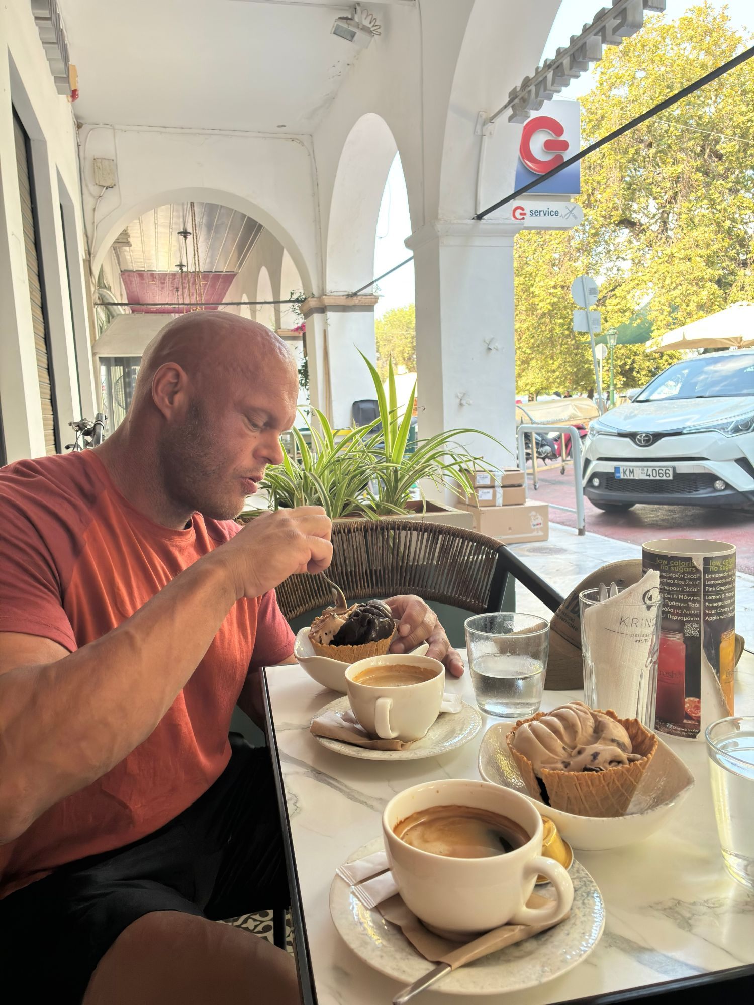 Eating ice cream in a waffle cup with coffee at a café table under white arcades in Pylos